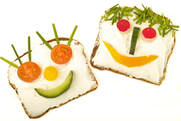 Two pieces of open-face bread decorated with various vegetables in order to look like they have faces